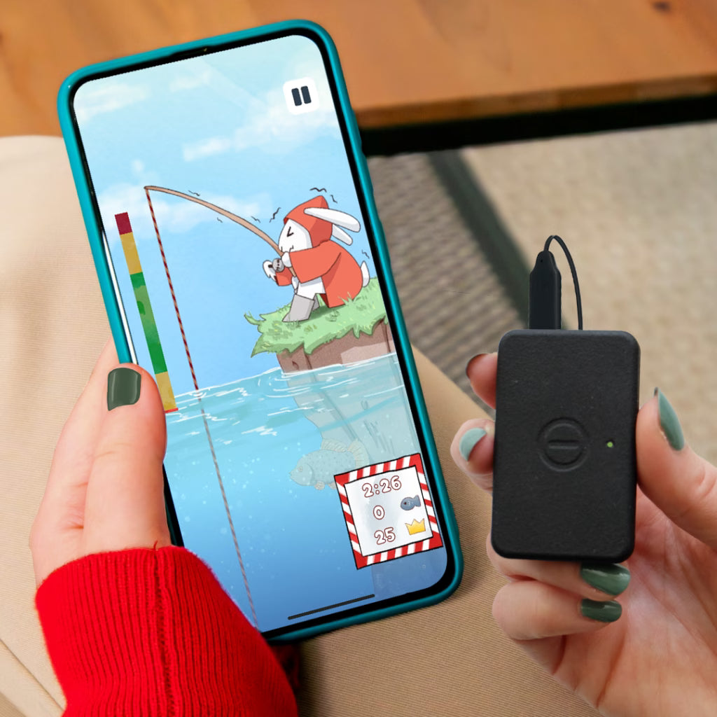Person holding a smartphone with a fishing game and a small black device.