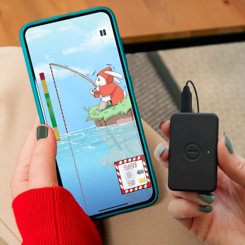 Person holding a smartphone with a fishing game and a small black device.